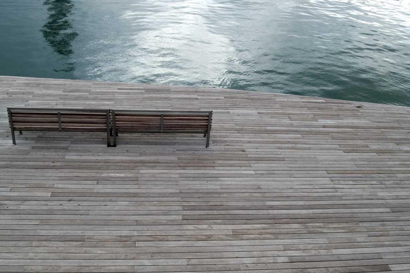 Two wooden benches on a boardwalk at the very edge of open water.
