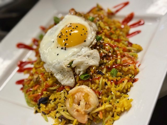 Fried rice with shrimp and a fried egg on top, streaked with chilli sauce, on a white rectangular plate.