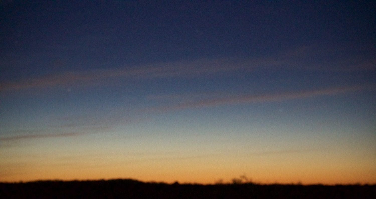 A wide dusk sky, orange fading up into deep blue over a flat dark horizon.
