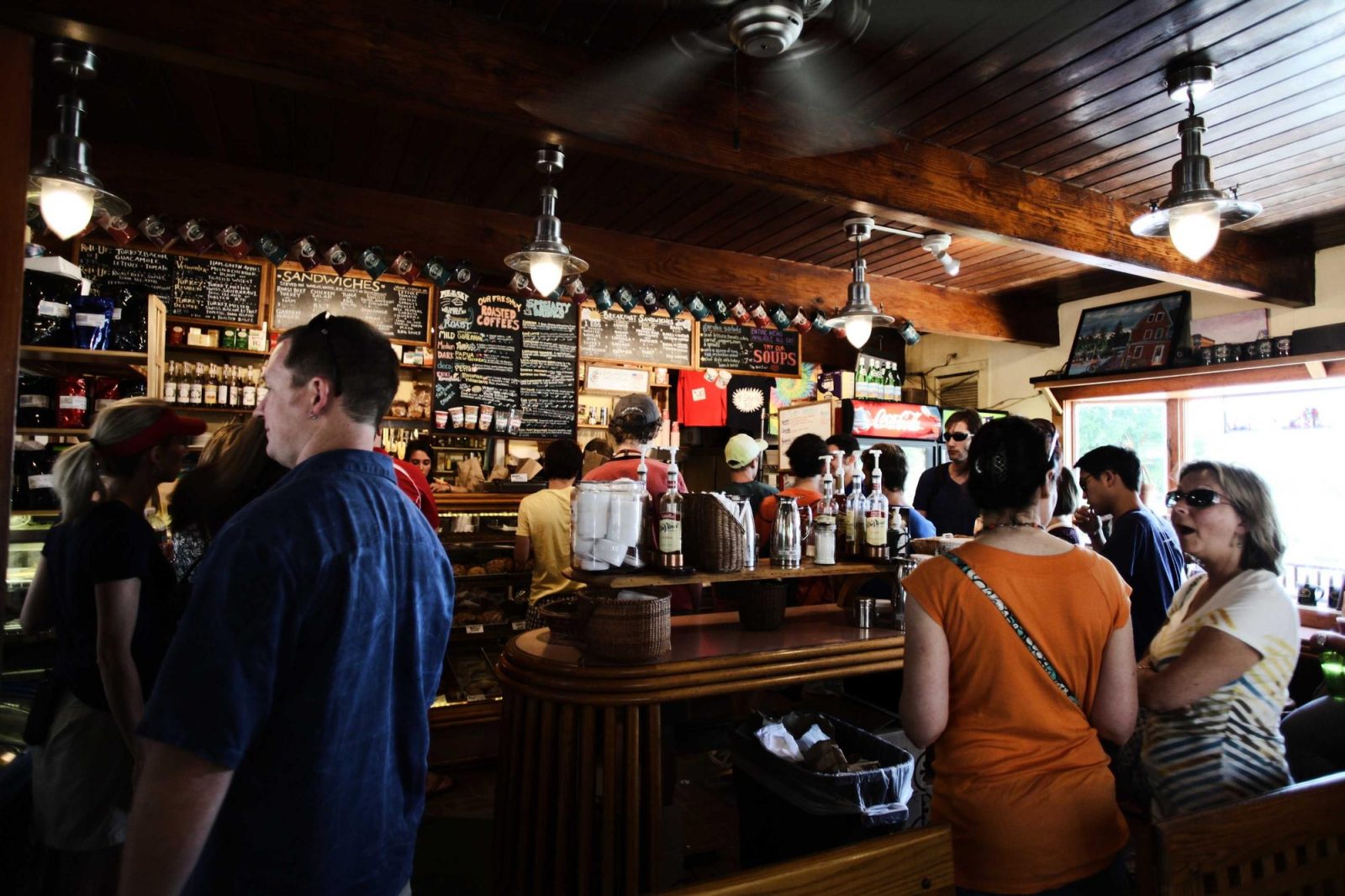 A busy bar on an evening — people standing and seated along the counter under warm pendant lights, bottles ranked behind.