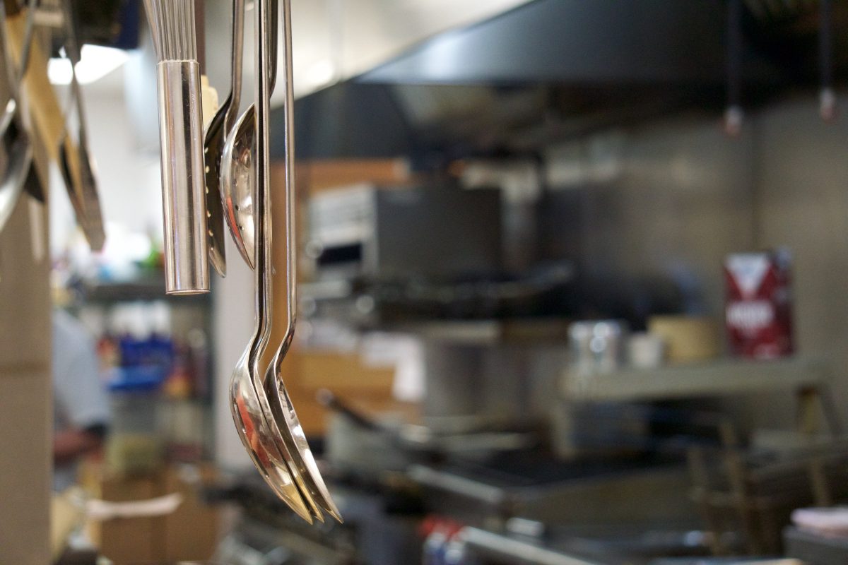 The Dockside kitchen — stainless steel surfaces with a rack of ladles and serving spoons hanging above the pass.